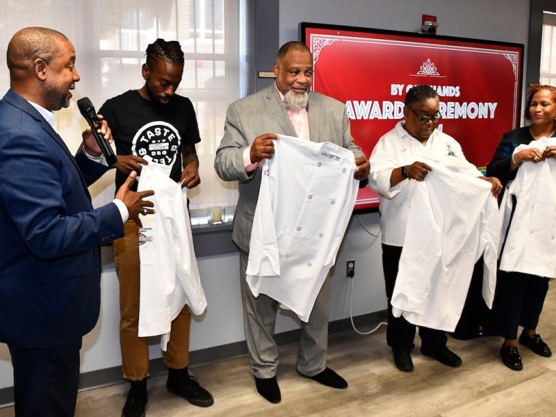 Furard Tate, executive director of entrepreneurship at the Greater Washington Urban League, awards Joseph McPherson, Reese Dixon, Leah Todd and Michelle Phipps with chef's tunics at the By Our Hands award ceremony on Sept. 21. (Robert R. Roberts/The Washington Informer)