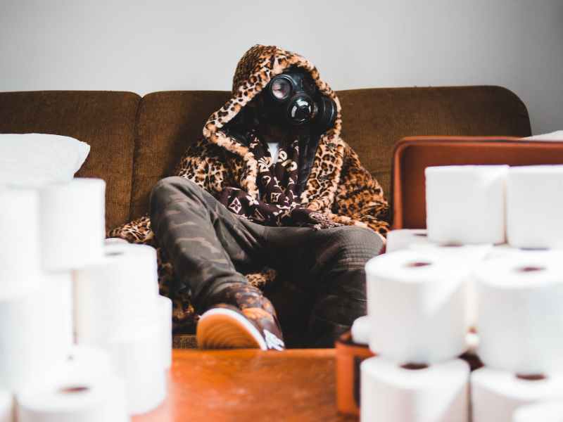 unrecognizable trendy man in respirator near pile of toilet paper