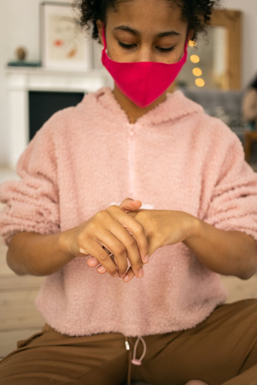 black girl in protective mask wiping hands with antiseptic